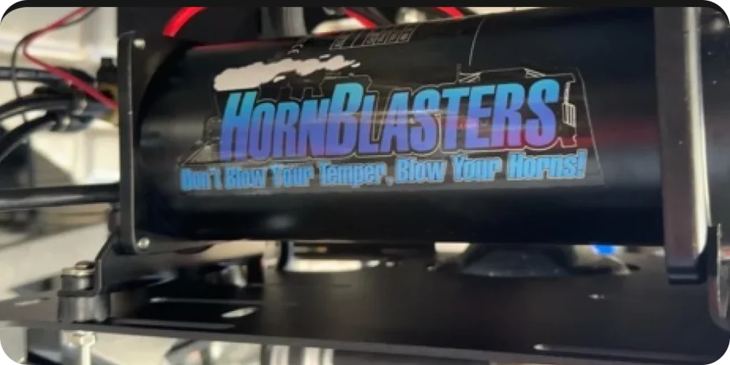 A black cylinder with the text: "HornBlasters. Don't Blow Your Temper, Blow Your Horns!" mounted on a metal frame.