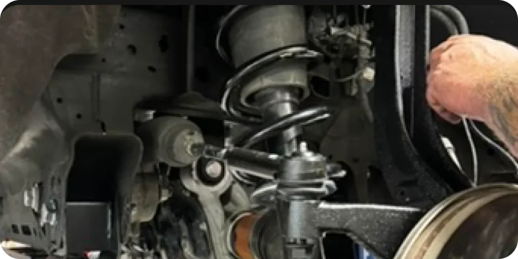 Close-up of a person working on the suspension system of a vehicle, with various mechanical parts visible.